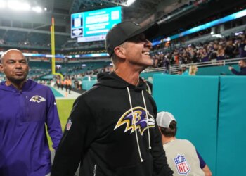 Baltimore Ravens head coach John Harbaugh smiles while walking off the field.