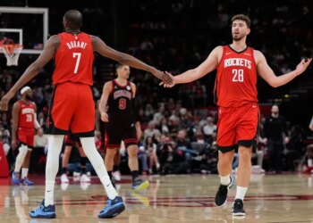 Two Houston Rockets players in red jerseys shake hands on the basketball court.