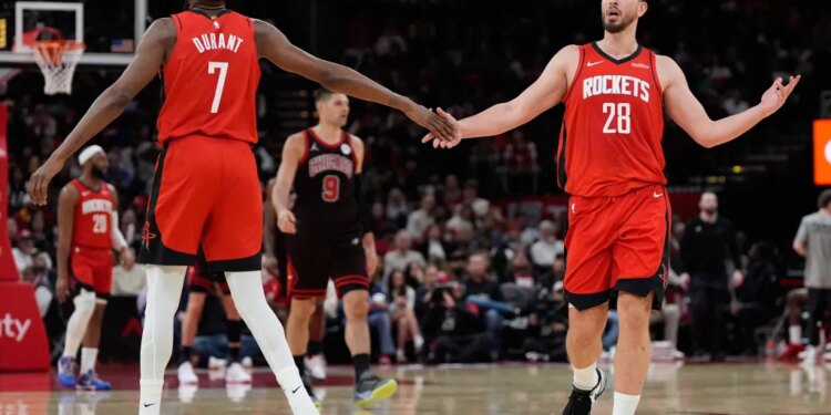 Two Houston Rockets players in red jerseys shake hands on the basketball court.