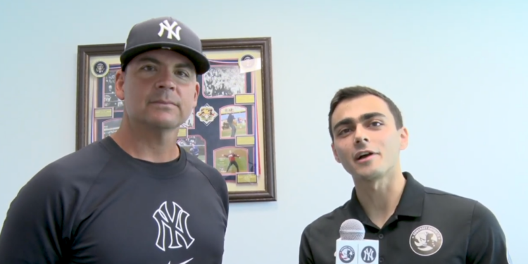 Two men, one in a Yankees cap and shirt and the other in a Somerset Patriots polo, stand in front of a framed display.
