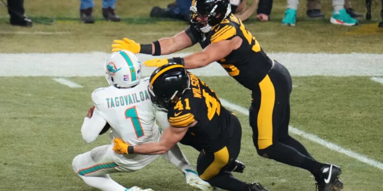 Tua Tagovailoa is sacked by Payton Wilson and Alex Highsmith during an NFL football game.