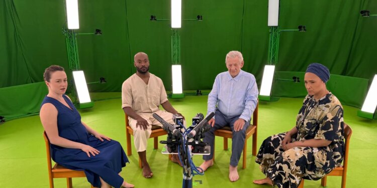 Two men and two women sitting in a semi circle on chairs. The room around the people is covered in green fabric, the floor is also green, and the group are all looking into an array of cameras.