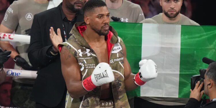 Boxer Anthony Joshua wearing white Everlast gloves and a camouflage vest, with a Nigerian flag behind him.