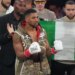 Boxer Anthony Joshua wearing white Everlast gloves and a camouflage vest, with a Nigerian flag behind him.