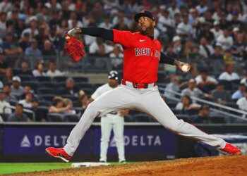 A Boston Red Sox pitcher in red and grey uniform throws a pitch.