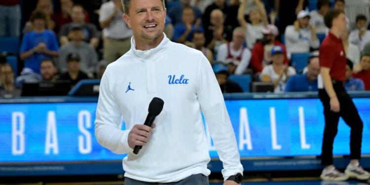 UCLA Bruins head football coach Bob Chesney holds a microphone at a basketball game.