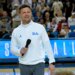 UCLA Bruins head football coach Bob Chesney holds a microphone at a basketball game.