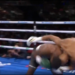 A boxer in black and white shorts falls to the mat while his opponent stands over him.