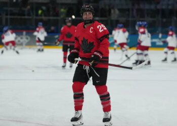 Marie-Philip Poulin of Canada in a red jersey and black helmet smiles during warmups at the 2026 Winter Olympics.