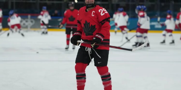 Marie-Philip Poulin of Canada in a red jersey and black helmet smiles during warmups at the 2026 Winter Olympics.