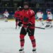 Marie-Philip Poulin of Canada in a red jersey and black helmet smiles during warmups at the 2026 Winter Olympics.