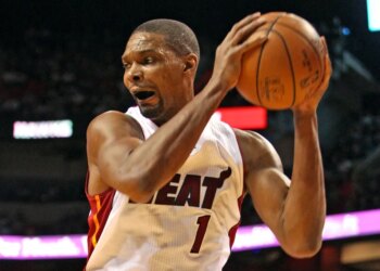 Basketball player Chris Bosh in a white "HEAT" jersey with number 1, holding a basketball with both hands and his mouth open, during a game.