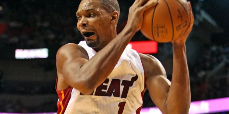 Basketball player Chris Bosh in a white "HEAT" jersey with number 1, holding a basketball with both hands and his mouth open, during a game.