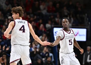 Two basketball players, one wearing jersey number 4 with the name "FOGLE" and the other wearing number 5 with "ZAGS", touch hands during an NCAA basketball game.
