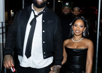 Trent Williams and a woman hold hands, smiling while walking at night.