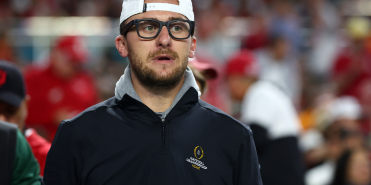 A man wearing a white cap backwards, glasses, and a black jacket with a "National Championship Miami" logo.