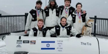 Members of Israel's Winter Olympics bobsleigh team, with Adam “AJ” Edelman (right), posing with their bobsled and a dog.