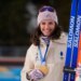 Julia Simon, of France, smiles while holding her gold medal from the women's 15-kilometer individual biathlon race and two pairs of skis.