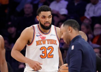 Karl-Anthony Towns with a cut near his right eye and blood on his jersey, being checked by a trainer.