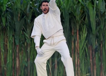 Bad Bunny performing during the Super Bowl halftime show, wearing a white outfit and pointing up.