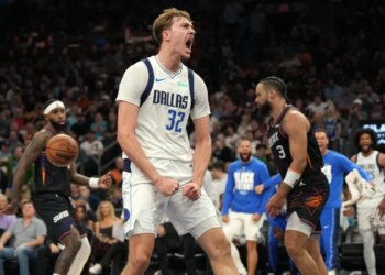 Dallas Mavericks player Davis Bertans shouts in celebration, fists clenched, after making a basket, with a Phoenix Suns player behind him.