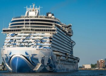 The cruise ship Norwegian Prima in blue and white, with "NORWEGIAN PRIMA" on its side, sailing on blue water.