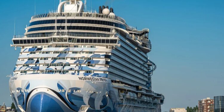 The cruise ship Norwegian Prima in blue and white, with "NORWEGIAN PRIMA" on its side, sailing on blue water.