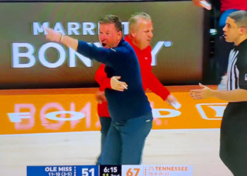 A basketball coach with his arm around another coach points and yells at a referee.