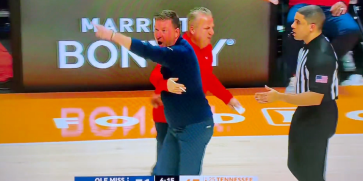 A basketball coach with his arm around another coach points and yells at a referee.