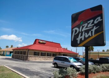 A Pizza Hut restaurant with a red roof and a large sign in the foreground, located in Florida, USA.