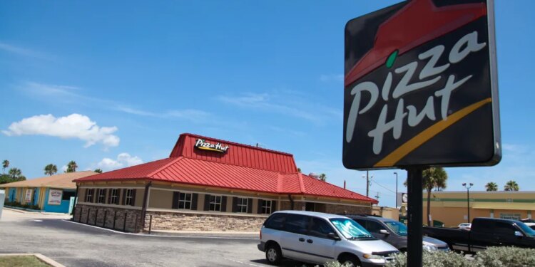 A Pizza Hut restaurant with a red roof and a large sign in the foreground, located in Florida, USA.