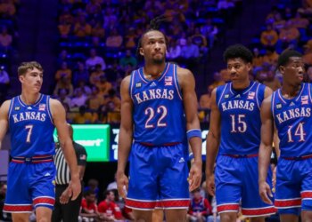Four Kansas basketball players in blue uniforms standing on the court.
