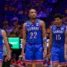Four Kansas basketball players in blue uniforms standing on the court.
