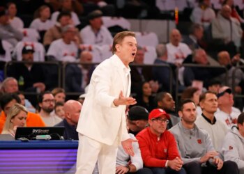 St. John's Red Storm head coach Rick Pitino in a white suit reacting on the sideline during a basketball game.