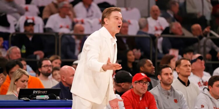 St. John's Red Storm head coach Rick Pitino in a white suit reacting on the sideline during a basketball game.