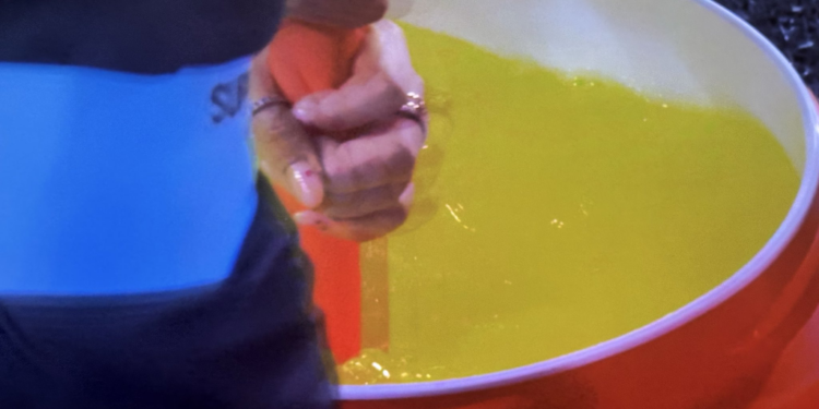 A person pouring yellow liquid into a red bucket.