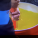 A person pouring yellow liquid into a red bucket.