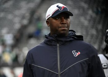 A man wearing a white Houston Texans baseball cap and dark blue jacket looks to the right.