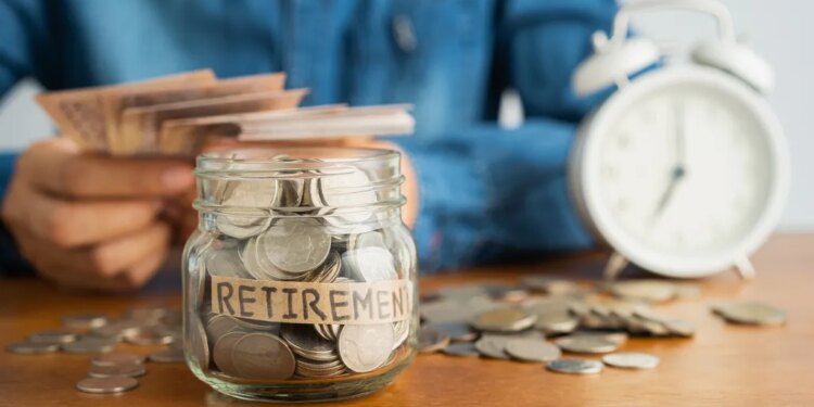 A person putting money into a glass jar labeled "RETIREMENT," with more money and an alarm clock in the background.
