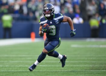 A Seattle Seahawks player in a dark blue uniform running with the football during a game.