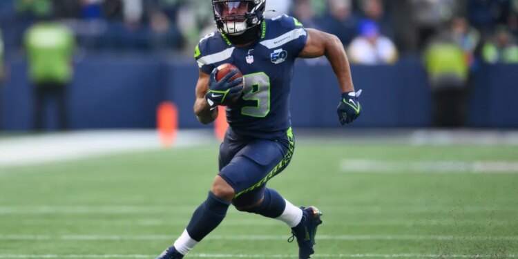 A Seattle Seahawks player in a dark blue uniform running with the football during a game.