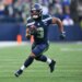 A Seattle Seahawks player in a dark blue uniform running with the football during a game.