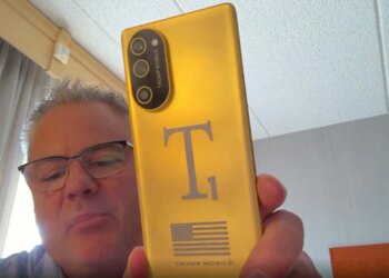 Screenshot of Eric Thomas from Trump Mobile holding a gold T1 Phone towards his webcam
