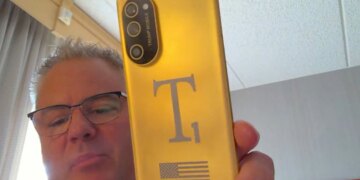 Screenshot of Eric Thomas from Trump Mobile holding a gold T1 Phone towards his webcam