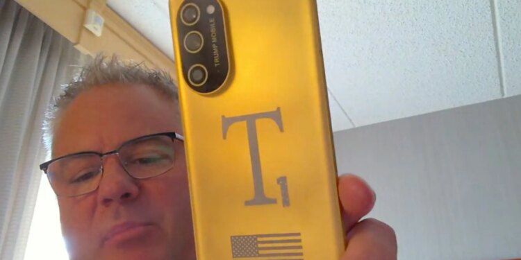 Screenshot of Eric Thomas from Trump Mobile holding a gold T1 Phone towards his webcam