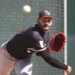 A baseball player in a black Twins cap and black jersey with a red glove winds up to pitch.
