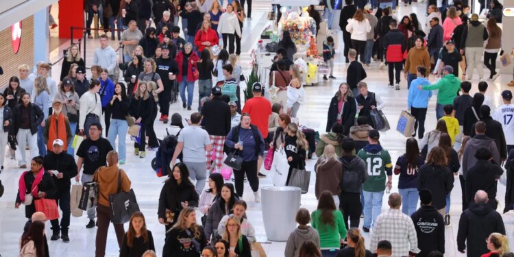 Shoppers fill a mall, carrying bags from Black Friday deals.