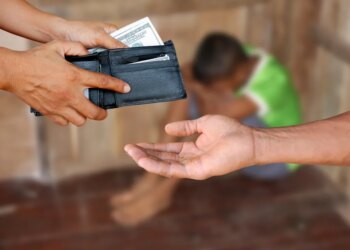A person's hands holding a wallet full of money over another person's open, dirty hand, with a third, sad, blurred person in the background, illustrating human trafficking.
