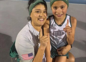 Emelie Chavez, the 7-year-old world record holder in the 3000M, and an adult pose for a picture on a track, both holding up one finger to signify their accomplishment.