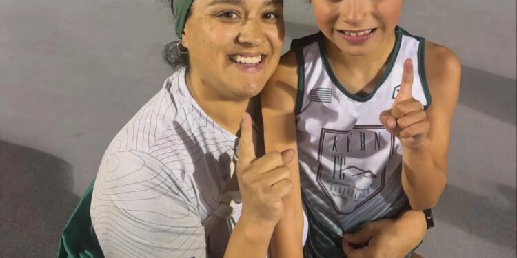 Emelie Chavez, the 7-year-old world record holder in the 3000M, and an adult pose for a picture on a track, both holding up one finger to signify their accomplishment.